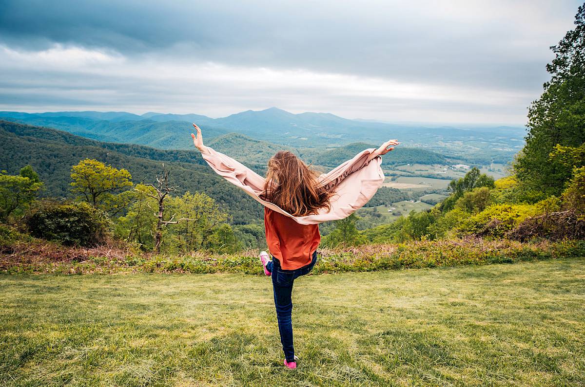 Teenage girl on top of a hill with her hands in the air