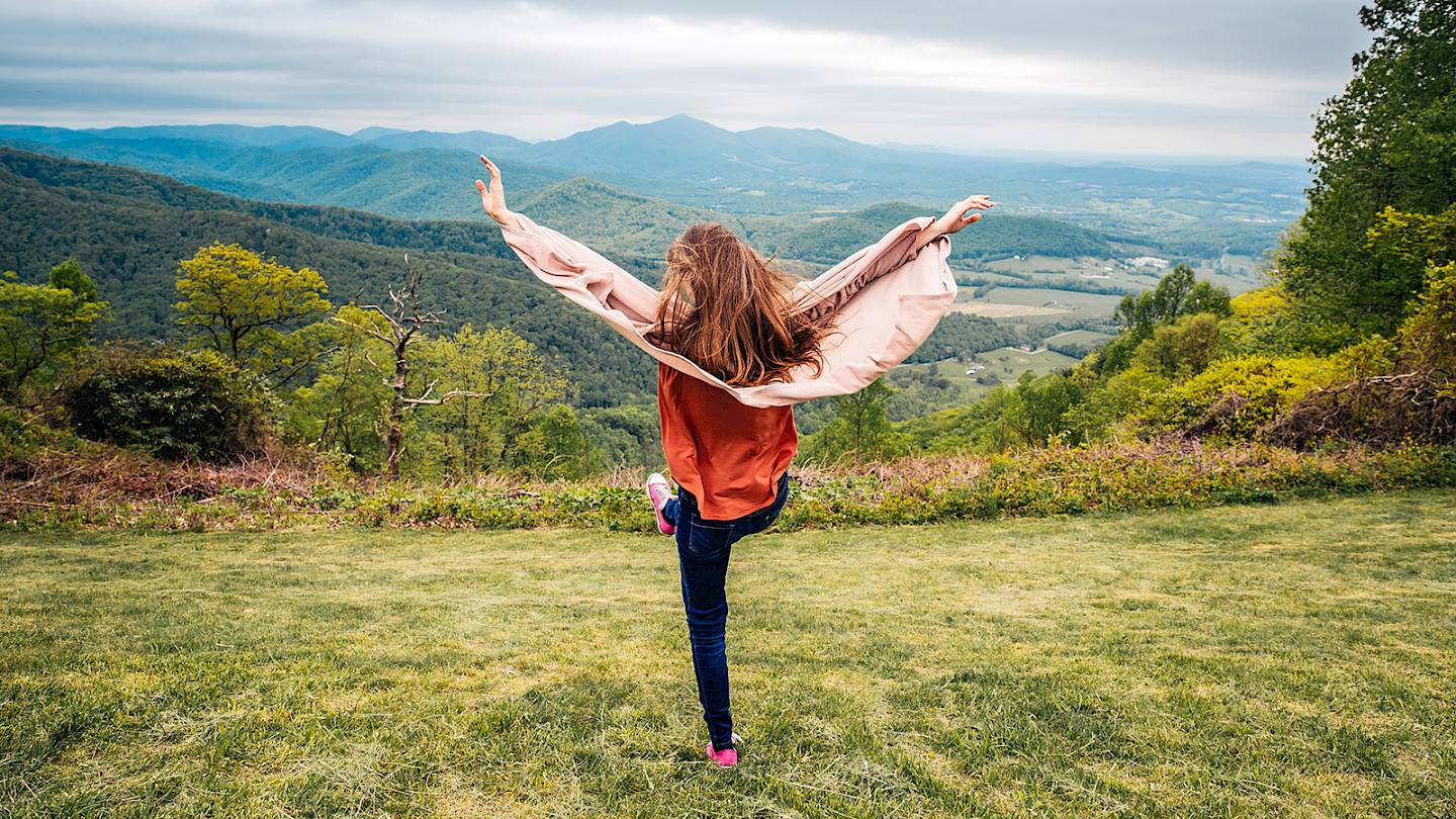 Teenage girl on top of a hill with her hands in the air