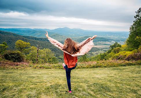 Young girl at the top of a hill catching the wind in her jacket